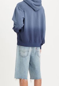 Felpa con cappuccio in blu sfumato, caratterizzata da una vestibilità comoda e polsini a costine, abbinata a pantaloni shorts in denim blu chiaro con orli sfilacciati.