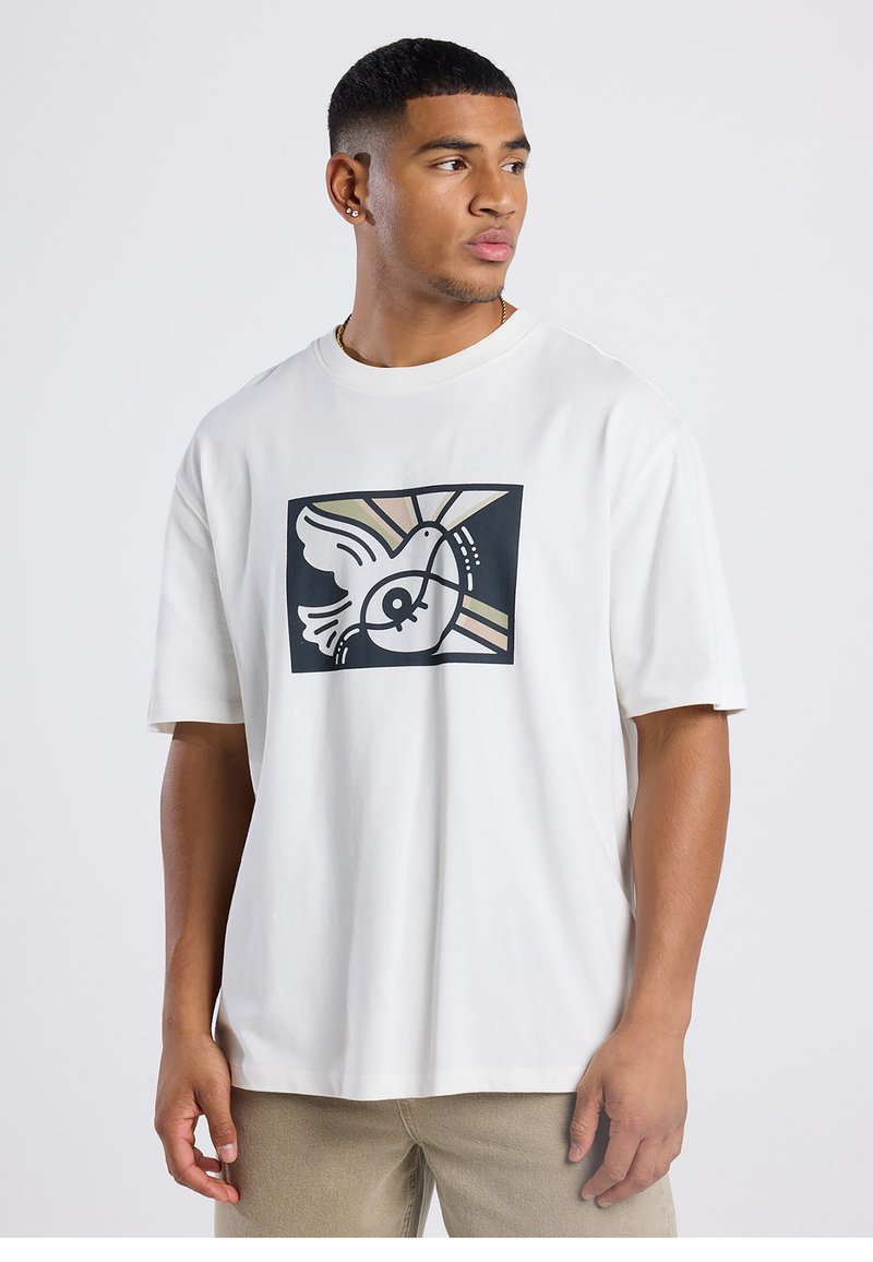 T-shirt blanc à manches courtes avec un motif graphique noir représentant un oiseau abstrait et des éléments géométriques aux couleurs pastel. Tissu doux.