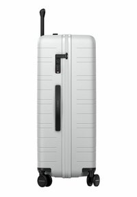 Valise rigide argentée avec une surface texturée, des lignes horizontales, une combinaison à verrou, une poignée et quatre roues noires pour la mobilité.