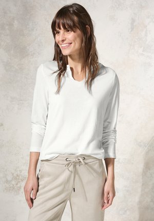 White long-sleeve top with a V-neck and relaxed fit, paired with light beige pants featuring a drawstring waist and a sleek texture.