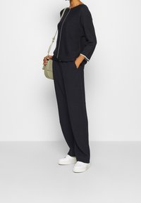 Ciemnogranatowy sweter z okrągłym dekoltem i kontrastowym białym szwem, w połączeniu z luźnymi granatowymi spodniami. Dodatek: mała zielona torebka.