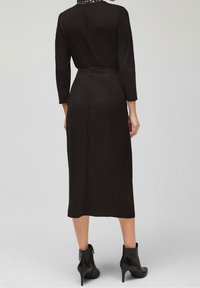 Czarna, do kolan sukienka z długim rękawem, o dopasowanym kroju i fakturowanym dekolcie. Noszona z czarnymi botkami na obcasie.