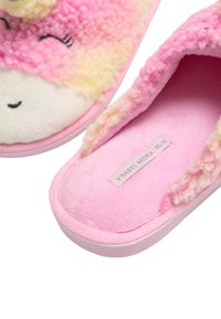 Zapatillas rosas y esponjosas con una textura suave, que presentan un diseño con una cara sonriente, detalles en blanco y una etiqueta que muestra la marca.