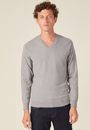 Suéter gris de cuello en v con mangas largas y diseño de punto texturizado. El suéter se ajusta al cuerpo, combinado con jeans de mezclilla oscura.
