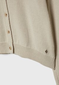 Beżowy sweter z dzianiny z dekoltem w serek, z pięcioma jasnobrązowymi guzikami i małym detalem z logo na dole. Żebrowane mankiety i dół.