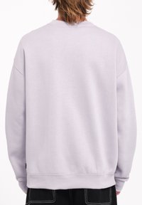 Sudadera de cuello redondo en gris claro con un corte relajado, puños y dobladillo de canalé, fabricada con una suave mezcla de algodón. Sin logos visibles.