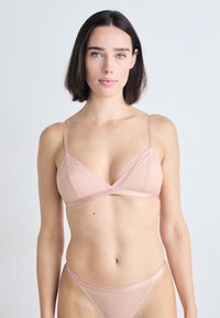 Bralette rosa com nervuras, alças finas ajustáveis, copas triangulares e fio dental minimalista a condizer. Textura suave e detalhes subtis.