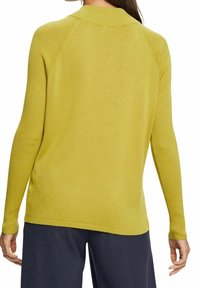 Pull à manches longues côtelé de couleur jaune vif, avec un col montant et une coupe légèrement ample, porté sur un pantalon bleu marine foncé.