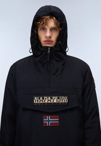 Zwarte waterdichte jas met een capuchon, uitgerust met een grote voorzak, een logo patch en een accent van de Noorse vlag. Glad weefsel.