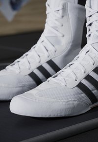 White athletic shoes with textured fabric and three black stripes on the sides. Features a padded cuff and a rubber sole for grip.