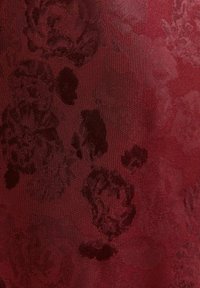 Bordowy materiał z subtelnym kwiatowym wzorem i teksturowaną powierzchnią. Wzór przedstawia ciemnoróżowe motywy kwiatowe, które stapiają się z tłem.