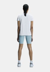 T-shirt de sport blanc à manches courtes et shorts ajustés bleu clair. Design simple avec une texture lisse. Comprend un détail de marque sur les shorts.
