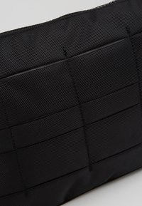 Borsa in tessuto nero con una trama a griglia. Presenta cuciture dettagliate e una finitura liscia e durevole. Chiusura con cerniera nella parte superiore.