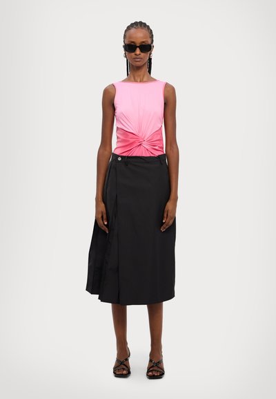 Fitted pink top with a twisted design at the center, paired with a black wrap skirt featuring a side button and a slit detail. Black strappy sandals.