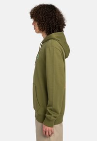 Olive green hooded sweatshirt with a kangaroo pocket, ribbed cuffs, and small graphic accents on the front and sleeve. Soft fabric texture.