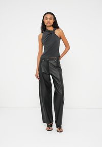 Zwarte mouwloze top met een gedraaide halslijn, gecombineerd met hoge zwarte leren wijde broek en open teen sandalen.