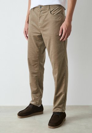 Khakifarbene Baumwollchinos mit geradem Bein, ausgestattet mit Vorder- und Hintertaschen, getragen mit dunkelbraunen Wildlederschuhen.