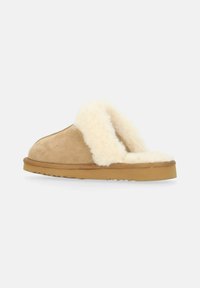 Beige mockasiner i mocka med ett krämfärgat fuskpälsfoder, öppen bakdesign och en gummisula med en texturerad yta för bra grepp.