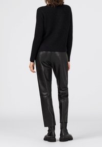 Svart stickad tröja med avslappnad passform, ihop med smala svarta läderbyxor och robusta svarta ankelstövlar. Släta texturer och minimalistisk design.