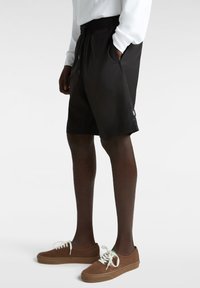 Schwarze Badeshorts mit elastischem Taillenbund und Kordelzug, ausgestattet mit seitlichen Taschen und einem kleinen Markenetikett am Saum.