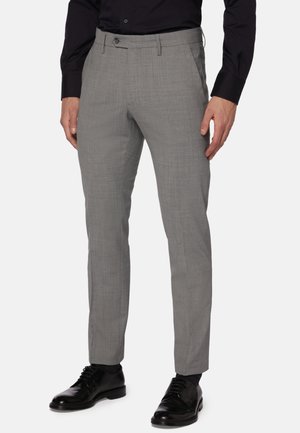 Pantalons tailleur gris avec une finition texturée, dotés d'une coupe classique et de plis sur le devant, associés à des chaussures en cuir noires.