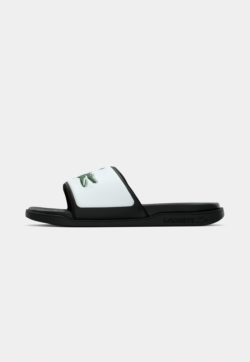 Sandale noire à glissière avec une sangle blanche arborant un logo crocodile Lacoste vert et une semelle texturée avec le branding Lacoste.