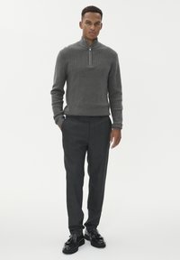 Siva pulover z zadrgo na vratu, lahka pletenina; krojene temno sive hlače z diskretnim vzorcem; črne poslovne čevlje z zaponko.