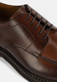 Bruine leren geklede schoenen met een gladde afwerking, voorzien van zes veterogen, subtiele stiksels en een gestructureerde zwarte rubberen zool.