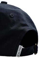 Gorra de béisbol azul marino con una tela texturizada, correa ajustable en la parte trasera y una pequeña etiqueta con "SCALPERS" visible en el costado.