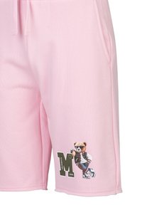Roze korte broek met zijzakken en een afbeelding van een beer die een zonnebril en een varsityjack draagt en leunt op een grote letter "M".