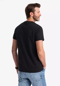 Camiseta negra de manga corta hecha de algodón, con escote redondo y una textura suave. Se lleva con jeans de color azul claro.