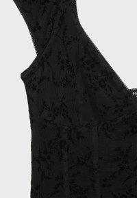 Haut noir sans manches avec motif en velours floral et tissu en mesh transparent sur fond clair.