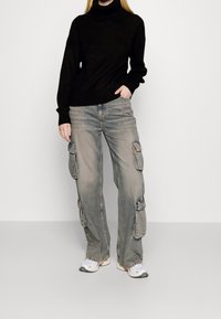Suéter negro de cuello alto de punto, combinado con jeans cargo gris claro que cuentan con bolsillos laterales y un corte relajado, complementado con zapatillas blancas.