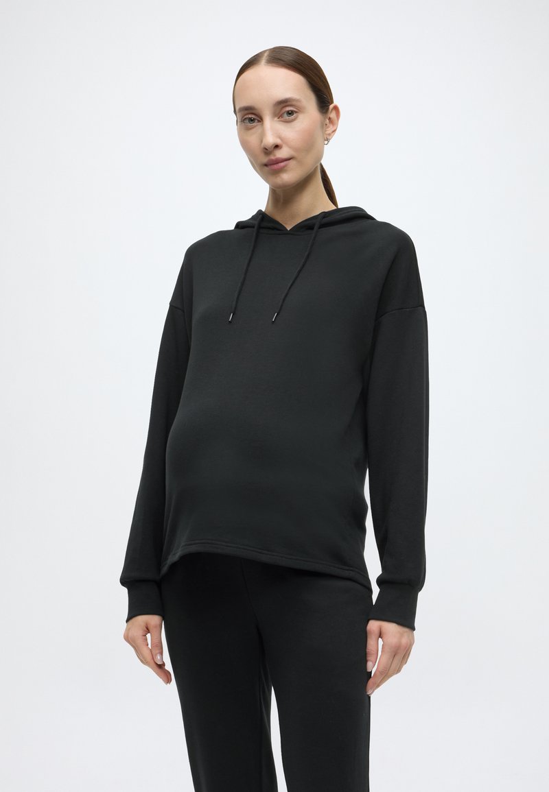 Czarna bluza z miękkiego materiału z kapturem na sznurki, luźnym krojem, długimi rękawami i bocznymi rozcięciami, zestawiona z dopasowanymi czarnymi spodniami.