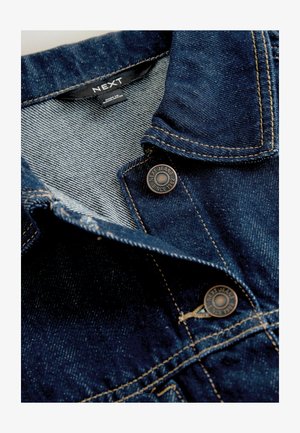 Sötétkék farmerdzseki strukturált felülettel, galléros nyakkal és bronz gombokkal, amelyeken a "NEXT JEANS SINCE 1982" felirat található.