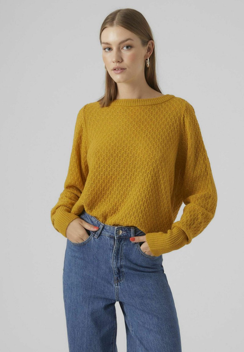 Geel gebreid sweater met een gestructureerd ruitpatroon, brede halslijn en losse mouwen, gecombineerd met hoog-getailleerde blauwe denim jeans.
