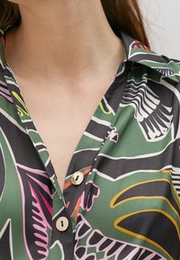 Camicia a maniche corte con bottoni, in tessuto verde con motivi astratti a foglia multicolore e bottoni dorati.