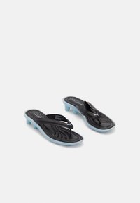 Black and blue Puma slide sandals with low block heels and thong straps on a white background.