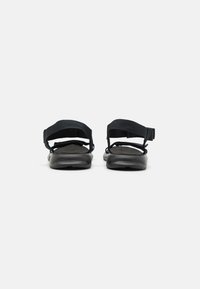 Black sandals featuring adjustable fabric straps and a molded rubber sole, showcasing a flat design and smooth texture.