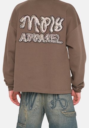 Bruine lange mouwen shirt met "MPly Apparel" geborduurd op de achterkant, gedragen met lichtblauwe spijkerbroek met donkere stikselontwerpen op de achterzakken.