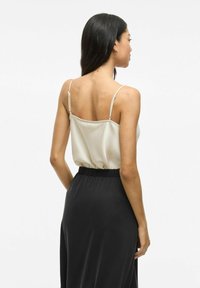 Lichtbeige satijnen top met verstelbare bandjes, gecombineerd met een zwarte rok met elastische taille. Gladde textuur, eenvoudig ontwerp.