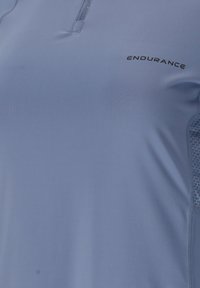 Hellblaues Sportshirt aus glattem, atmungsaktivem Material. Verfügt über einen kurzen Reißverschluss und ein gemustertes Mesh-Panel an der Seite. "ENDURANCE"-Logo sichtbar.