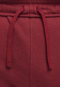 Maroon sweatpants with a textured cotton fabric. Features an elastic waistband, drawstring closure, and side seam pockets.