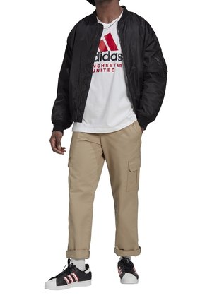 Musta bombaripusakka, valkoinen t-paita punaisella grafiikalla, beiget cargo-housut, mustat lenkkarit punaisilla yksityiskohdilla. Housujen lahkeet käännettyinä, näkyvät saumat.