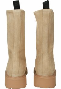 Botines de ante beige con una suela de plataforma gruesa marrón. Presentan una textura suave y una cinta en la parte trasera para ponerlos y quitarlos fácilmente. Diseño recto y minimalista.