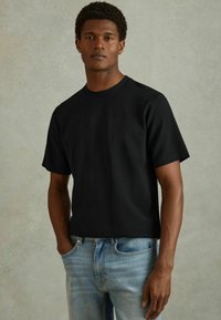 Tricou scurt negru din țesătură texturată, cu guler rotund. Asortat cu blugi de denim albaștri deschiși, cu croială dreaptă.