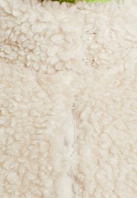 Krämfärgad fleece med en mjuk, strukturerad yta. Har en ljusgrön detalj upptill och en dold dragkedjestängning.