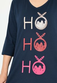 Marineblaues T-Shirt mit V-Ausschnitt, das drei "HO" Textdesigns zeigt. Jedes "O" ist ein dekoratives Ornament mit Stechpalmenakzenten in verschiedenen Farben.