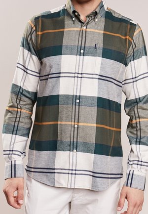 Mann trägt ein geknöpftes, langärmeliges kariertes Hemd mit grünen, weißen, grauen und orangefarbenen Streifen, kombiniert mit weißer Hose.