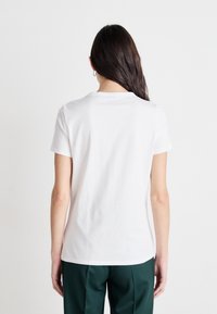 Camiseta de algodón blanca con un cuello redondo básico y mangas cortas. Presenta una textura suave y un corte relajado, vista desde la parte de atrás.